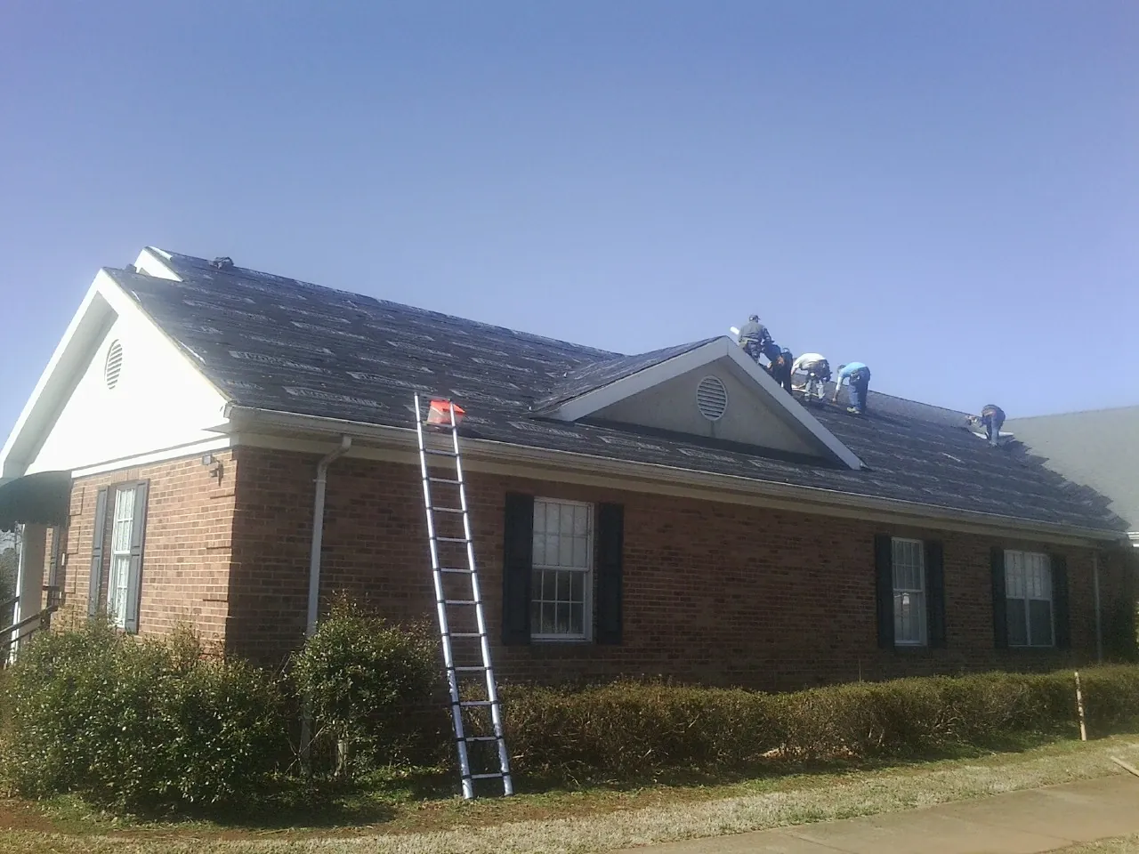 Crew tearing shingles off a brick ranch roof with a ladder set — Metal Roof Repair work by our crew in Newbury Park