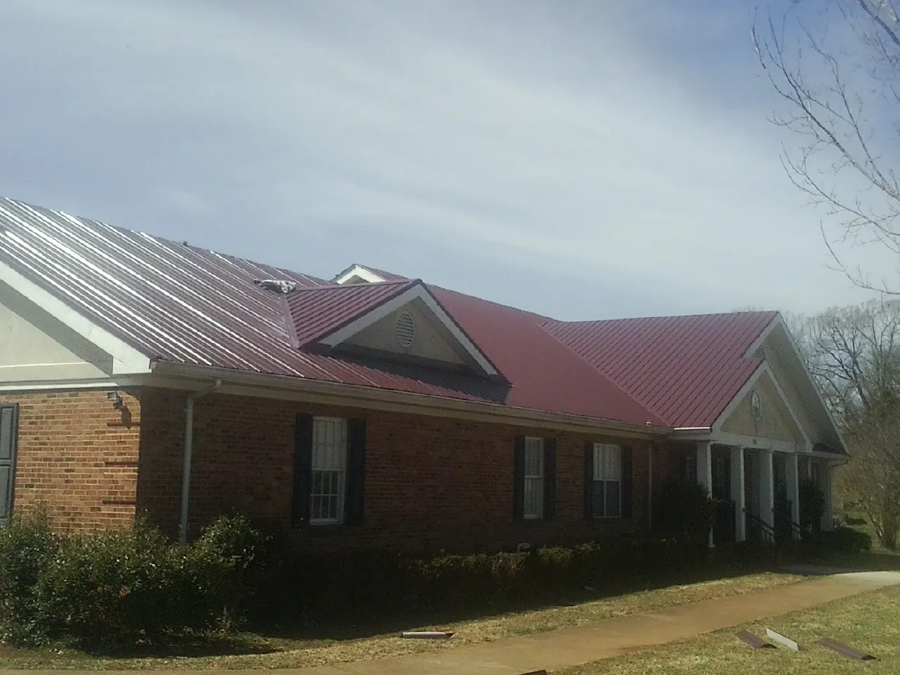Red metal roof with gabled entries on a long brick building, from a Hail Damage Roof Repair job in Newbury Park