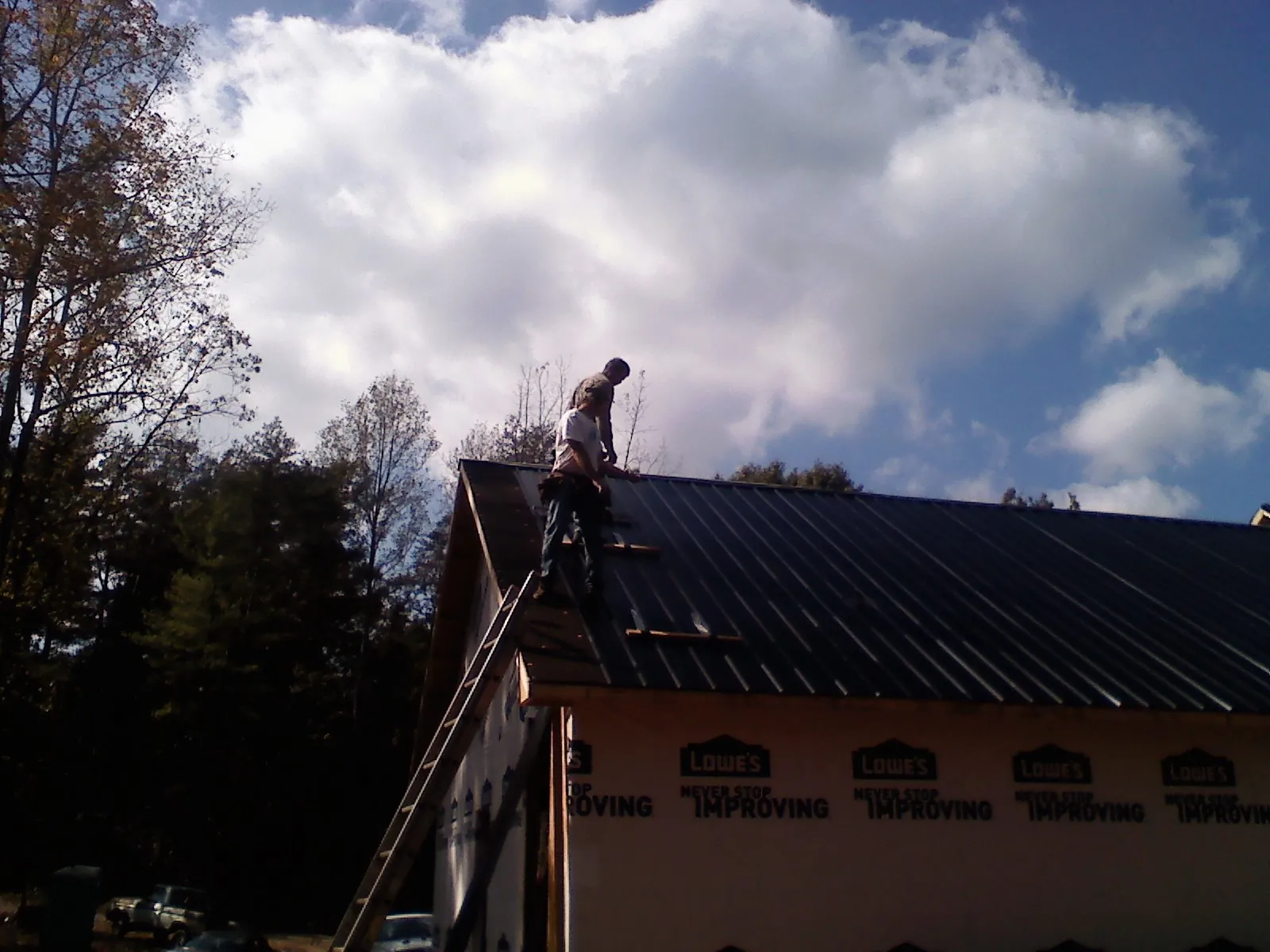 Roofer fastening dark metal panels high against a cloudy sky, from a Roof Inspection job in Newbury Park