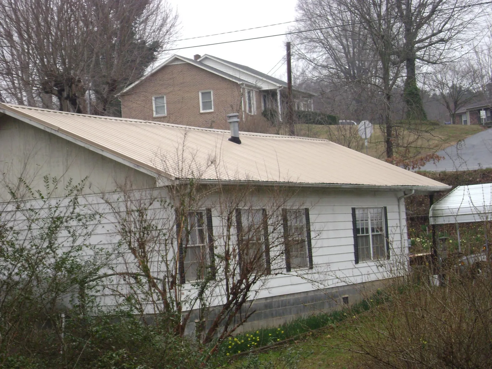 Tan metal roof on a white sided house set into a hillside — Commercial Roofing by Roofing Brothers in Newbury Park